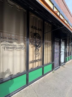 Street-side view of Aslan Acupuncture clinic windows displaying services and logo
